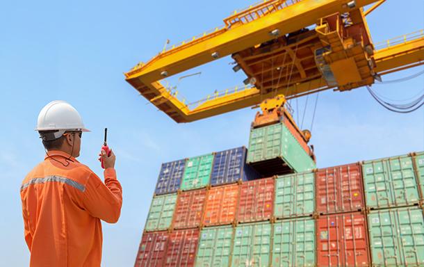 man working on shipping yard directing crane on walkie talkie while a shipping container is stacked