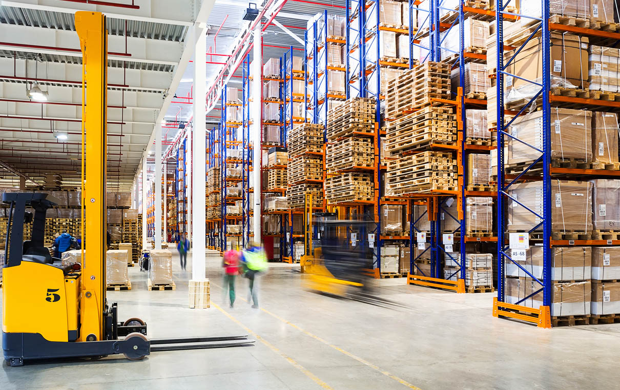 warehouse full of inventory with employees walking by and stacker lifts driving by